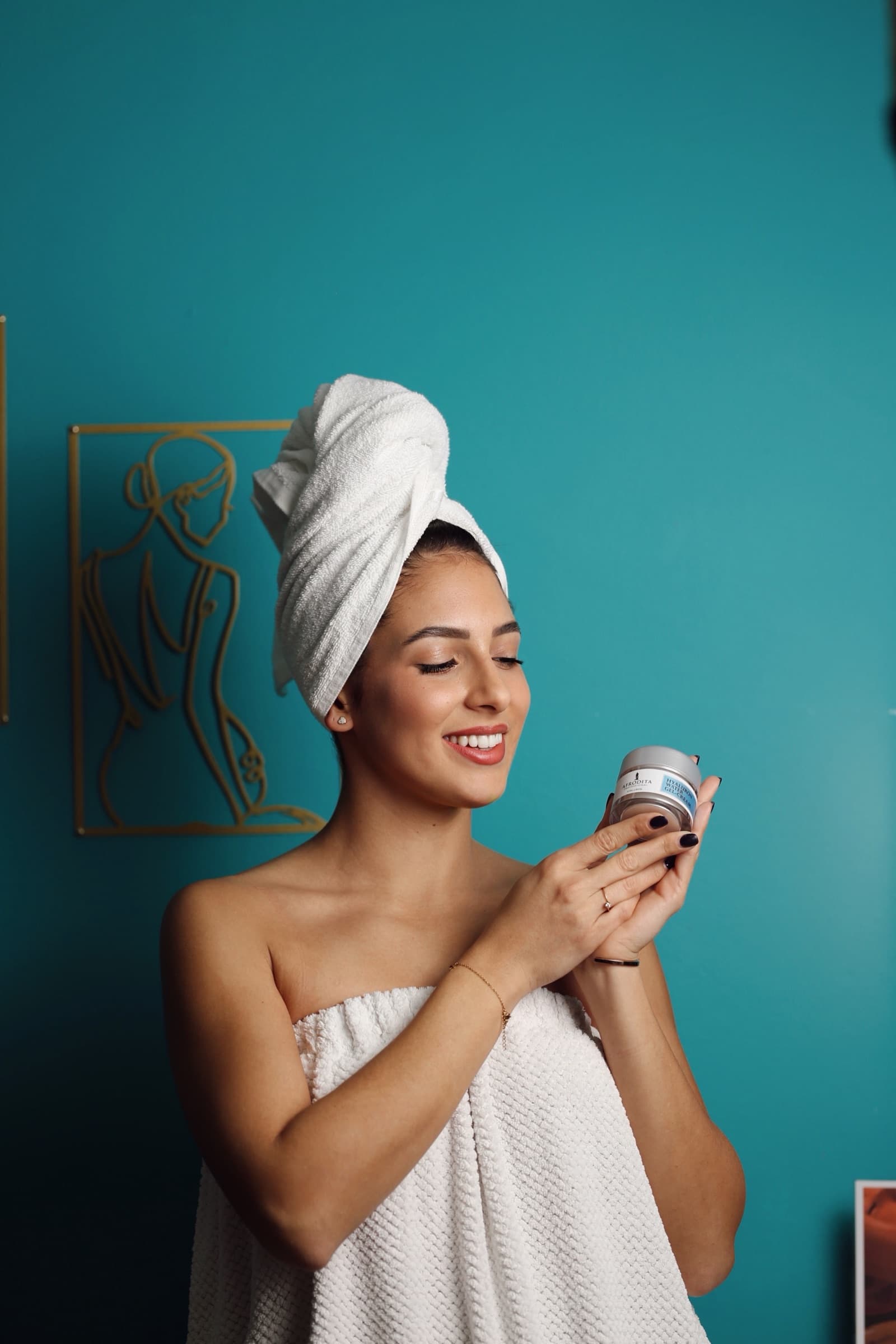Eyes closed with the cream jar, towel turban and teal backdrop
