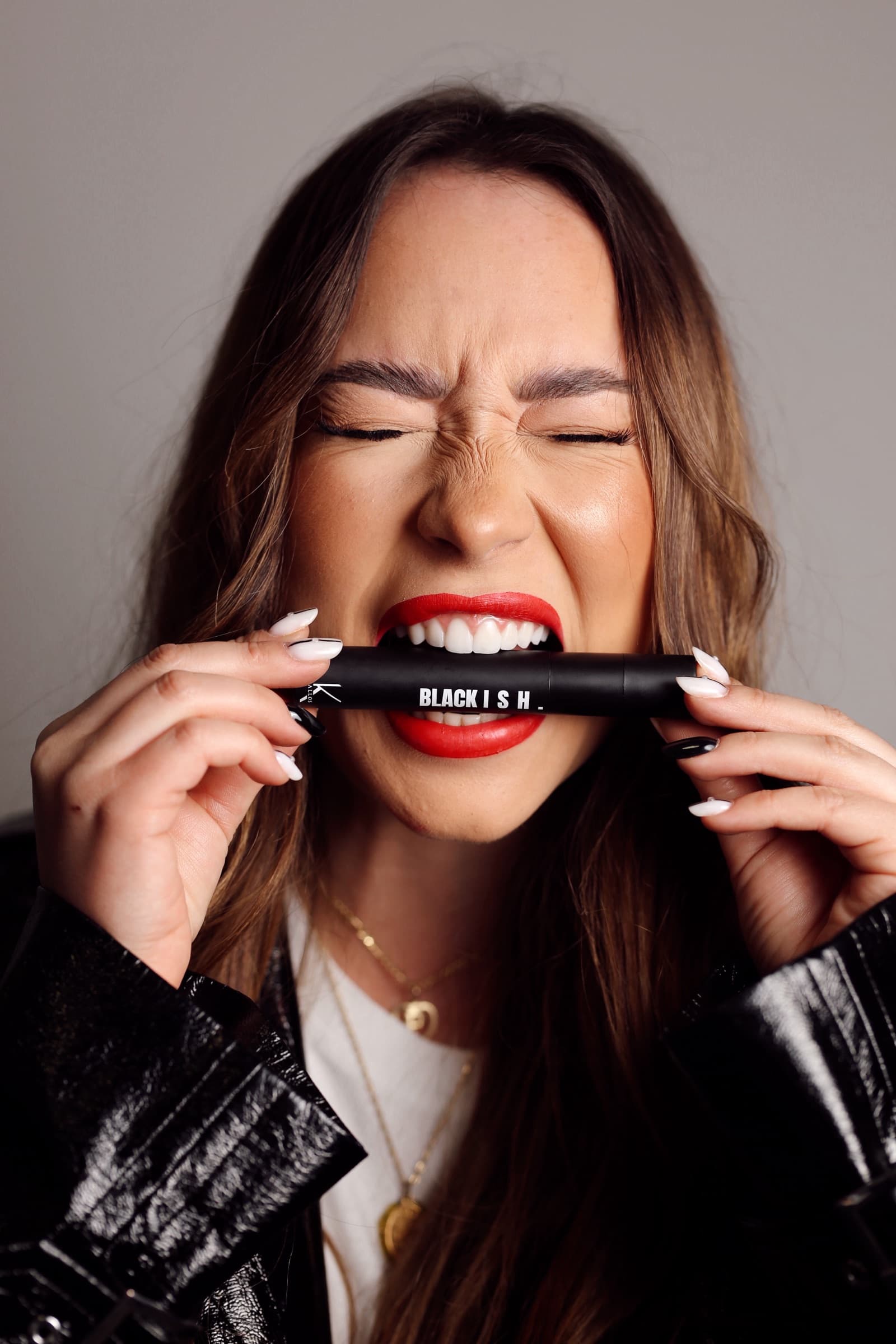 A Blackish cosmetics tube held between her teeth, red lip and leather jacket