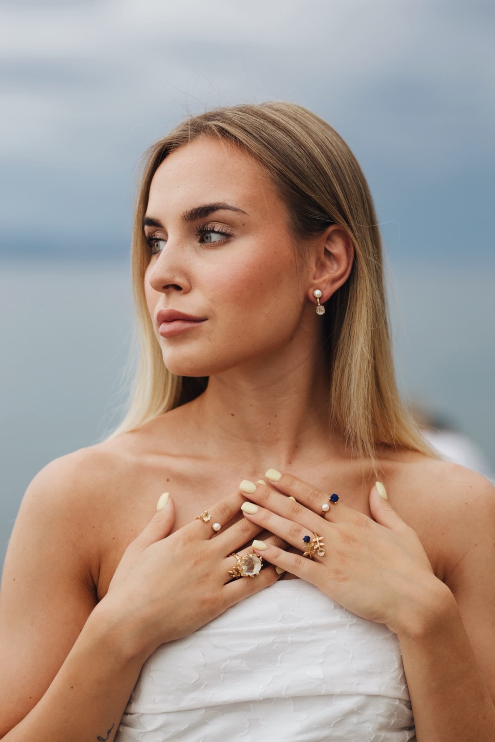Stacked Anka rings and pearl earrings, hands crossed at the chest