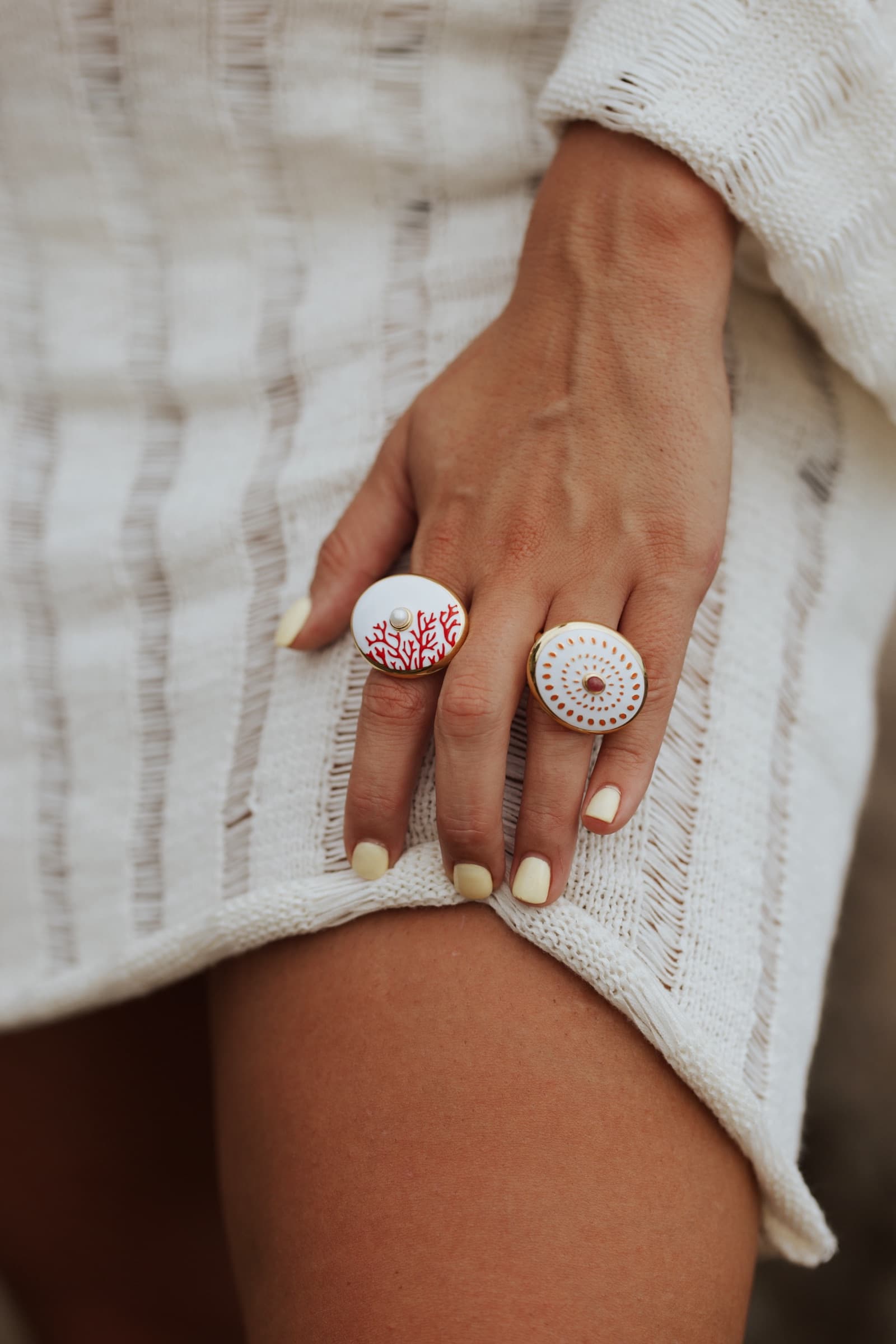 Two enamel Anka rings resting on white open knit