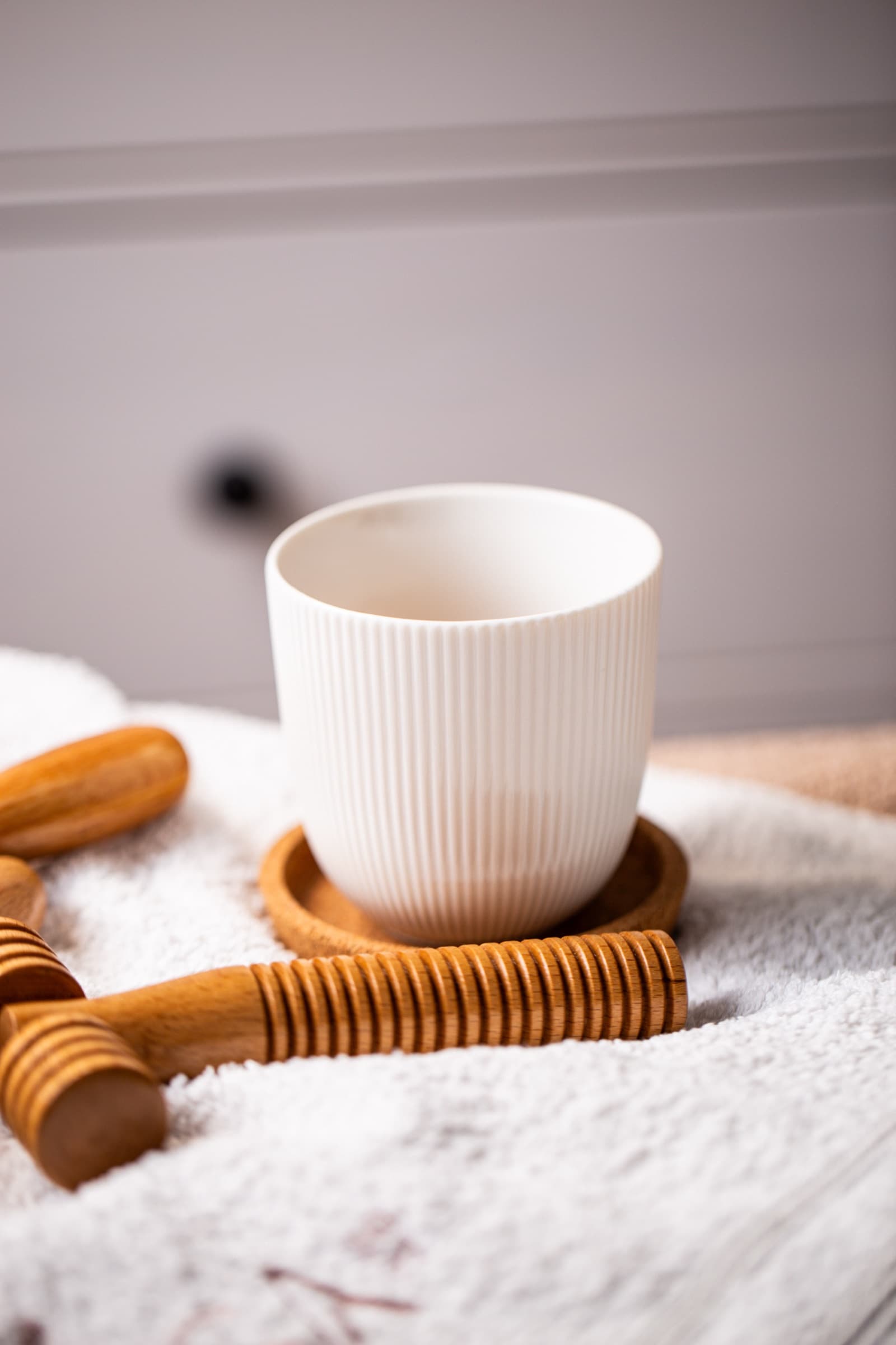 Ribbed ceramic cup and wooden rollers laid out on a white towel
