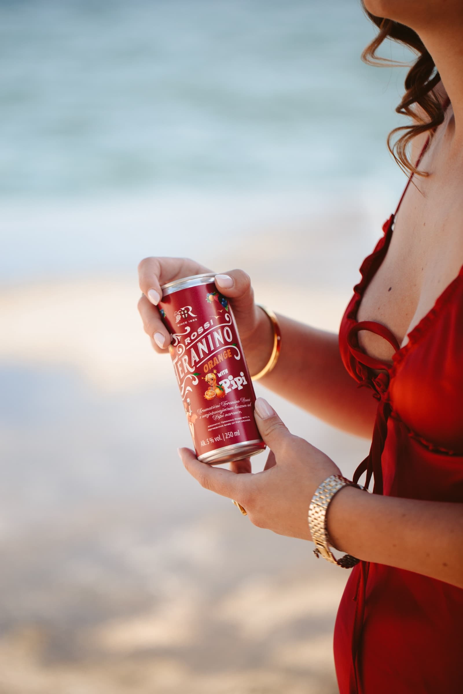 Teranino Orange can held against a red dress at the water's edge