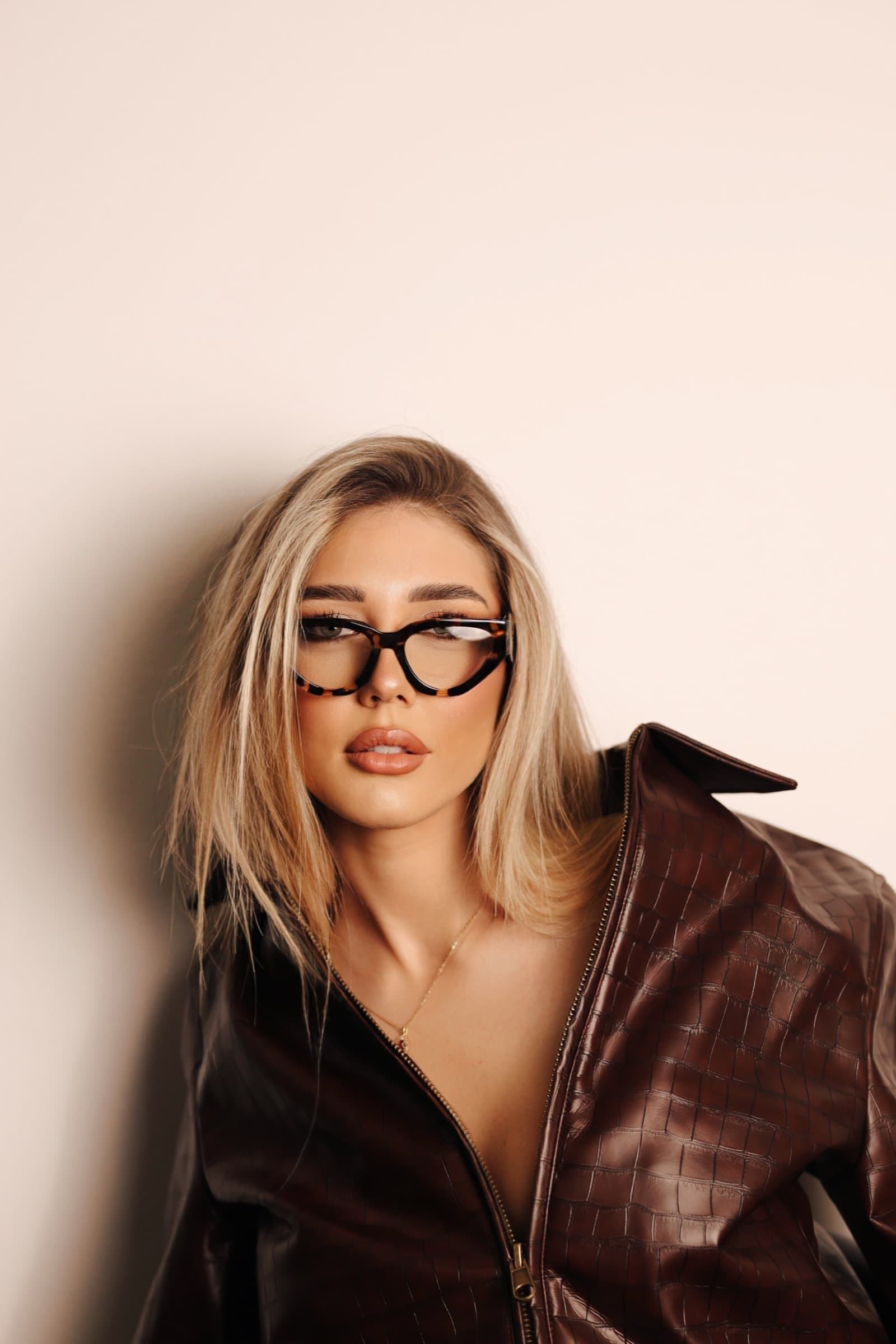 Blonde in brown leather with cat-eye frames, studio light