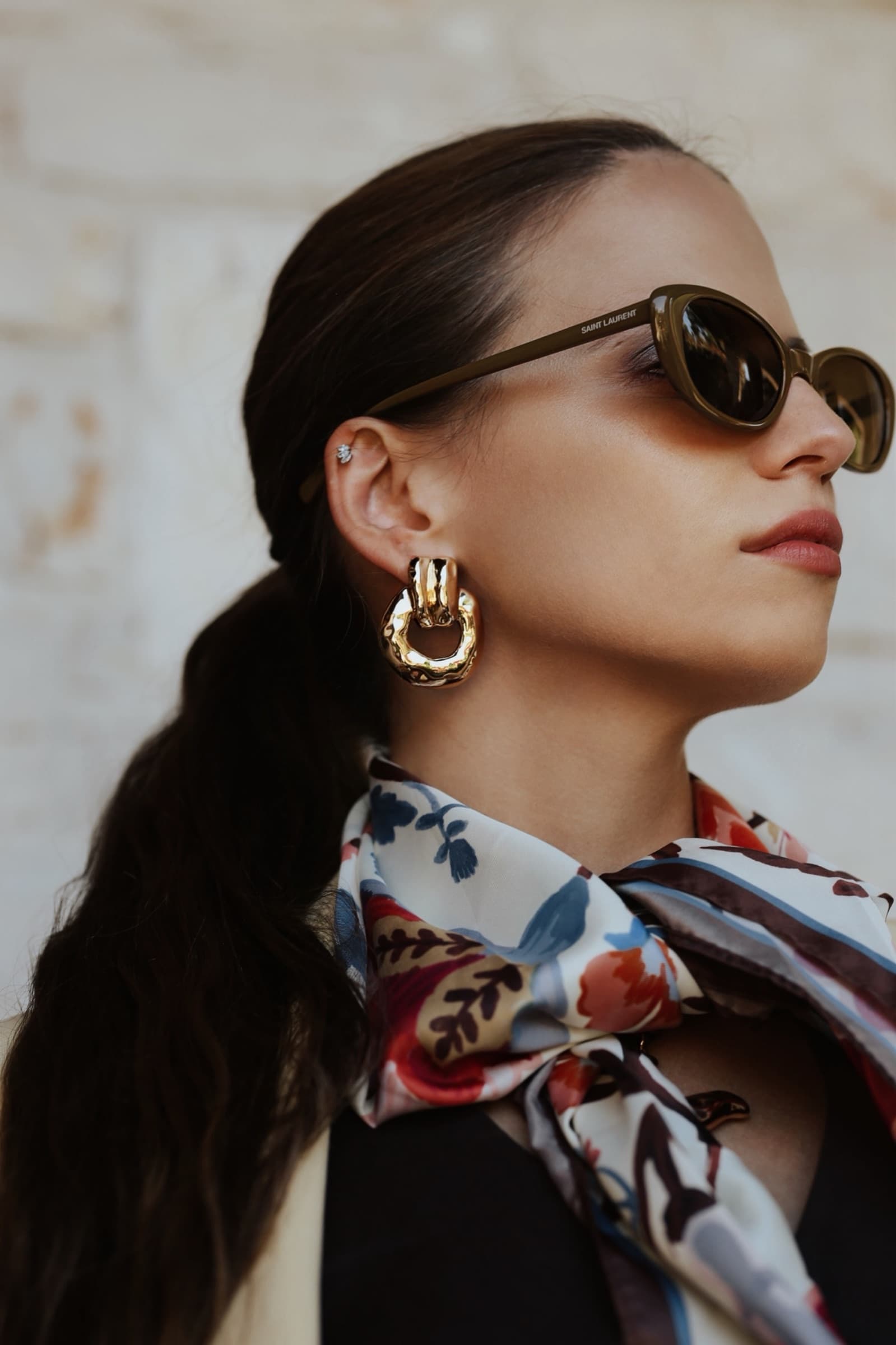 Oval sunglasses in profile with gold hoops and a silk scarf