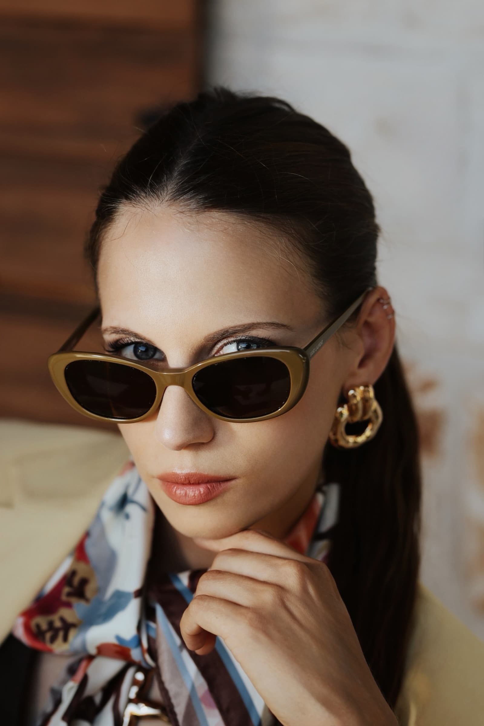 Olive-toned sunglasses framed by a printed silk scarf