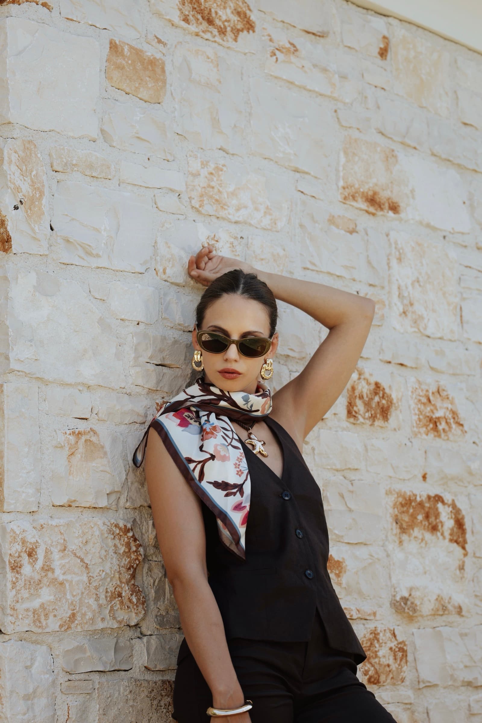 Leaning on the stone wall in sunglasses and a printed scarf