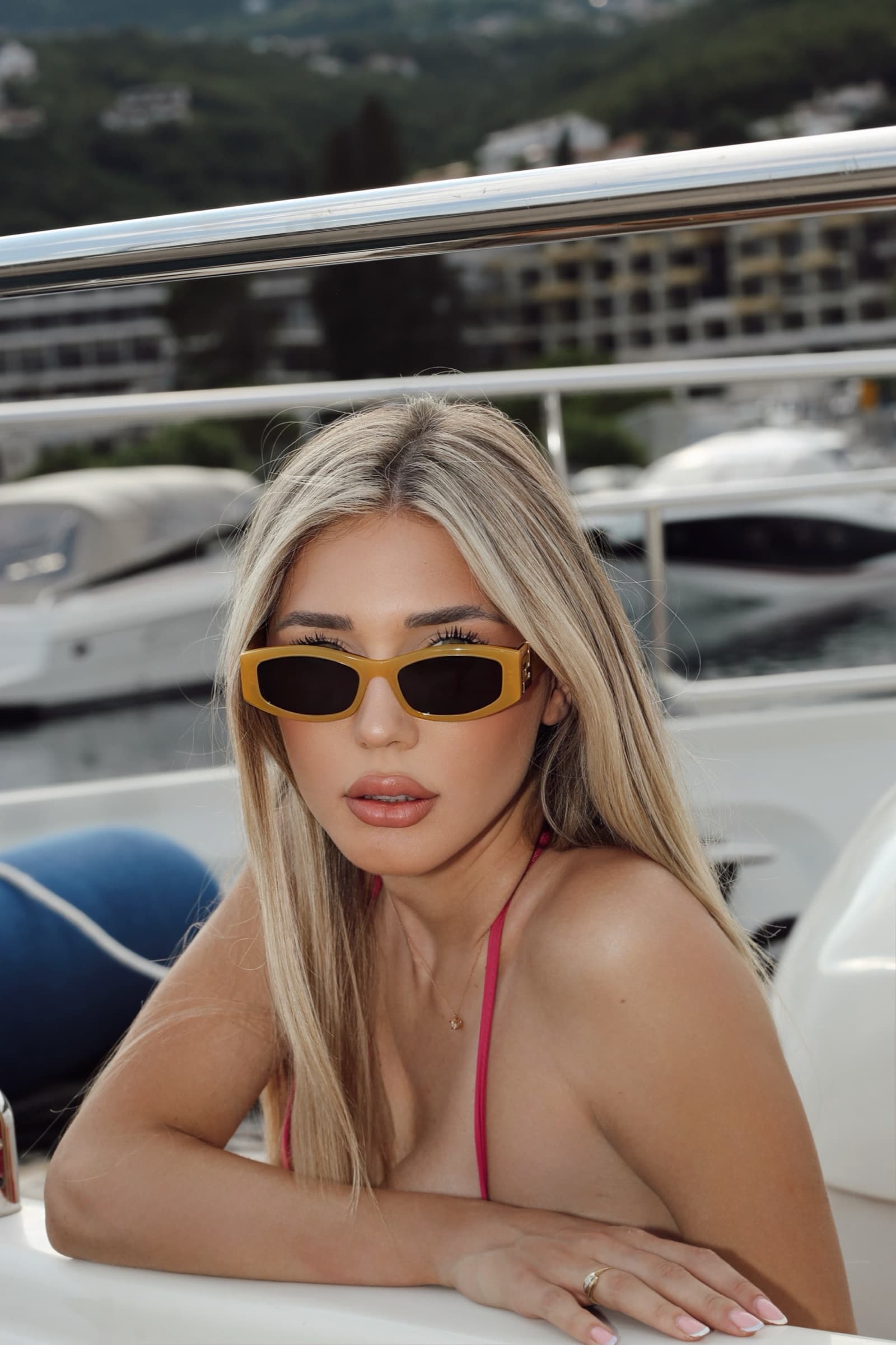 Leaning on the rail in yellow sunglasses, yachts behind