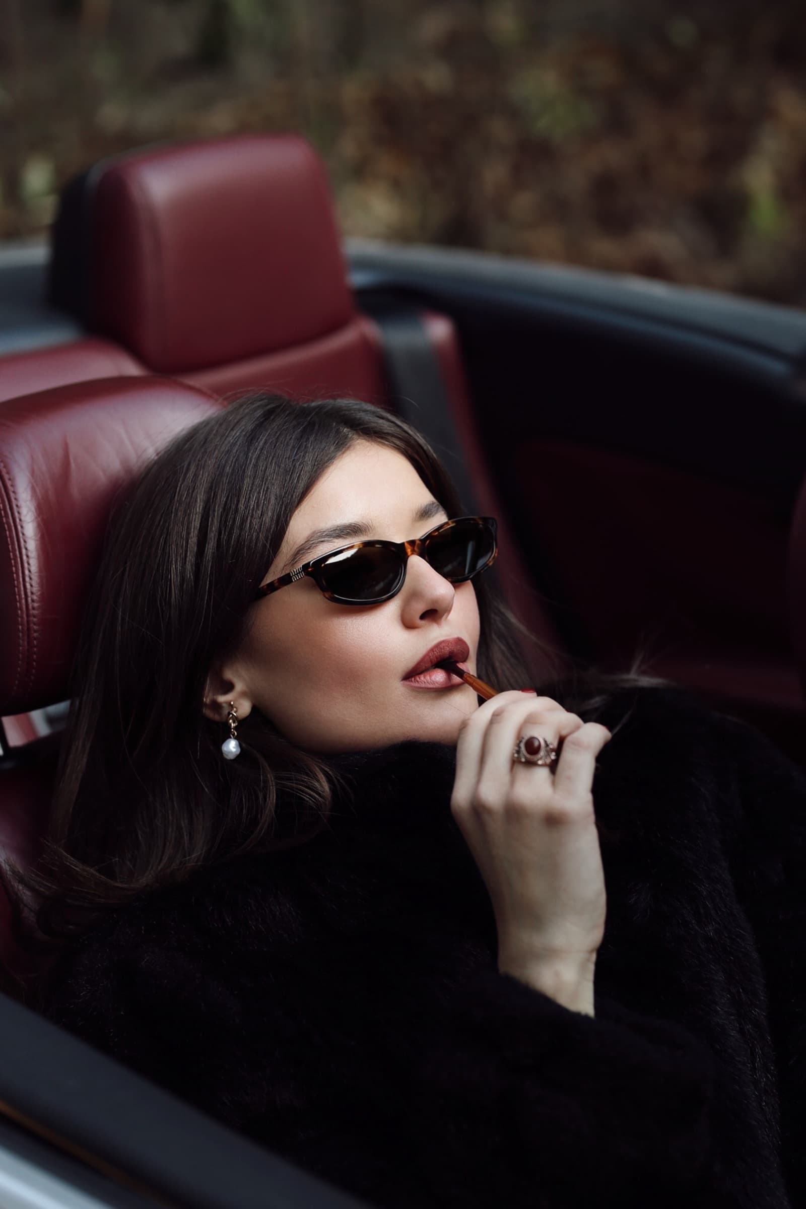 Small black sunglasses in the red leather seat of a convertible