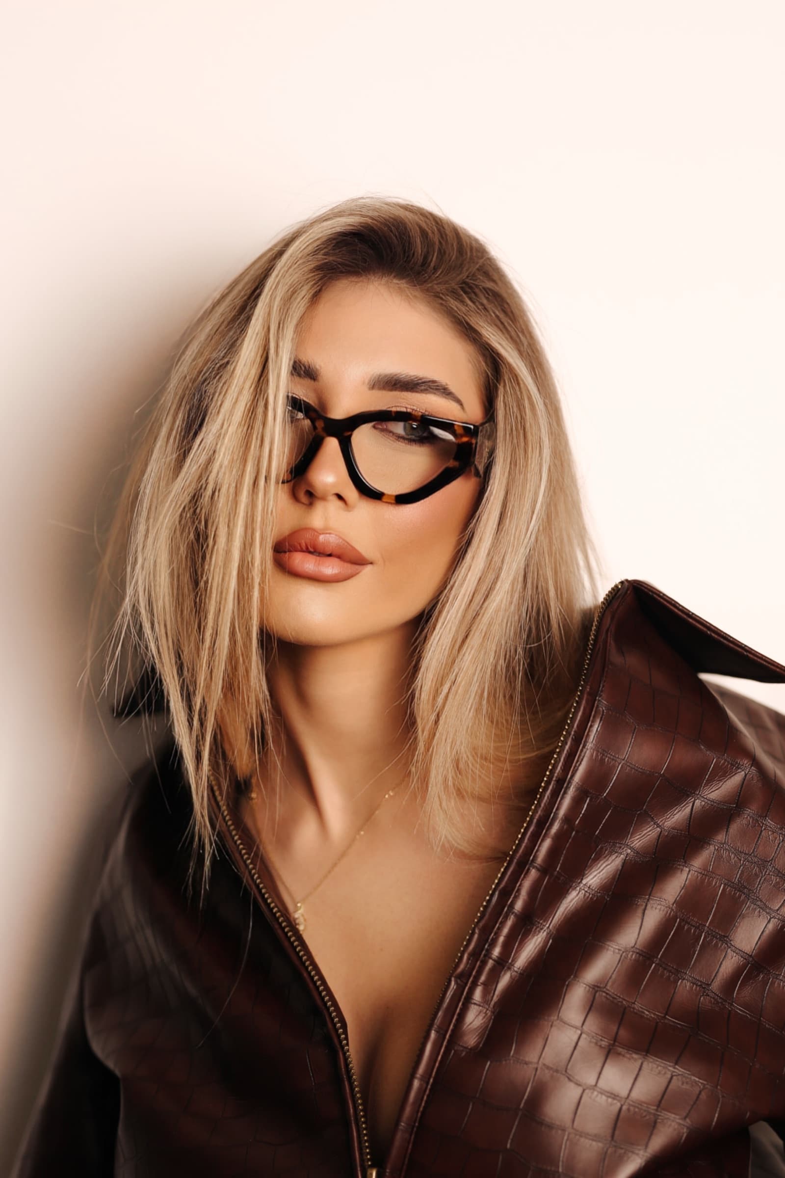 Blonde in brown leather with black optical frames, studio