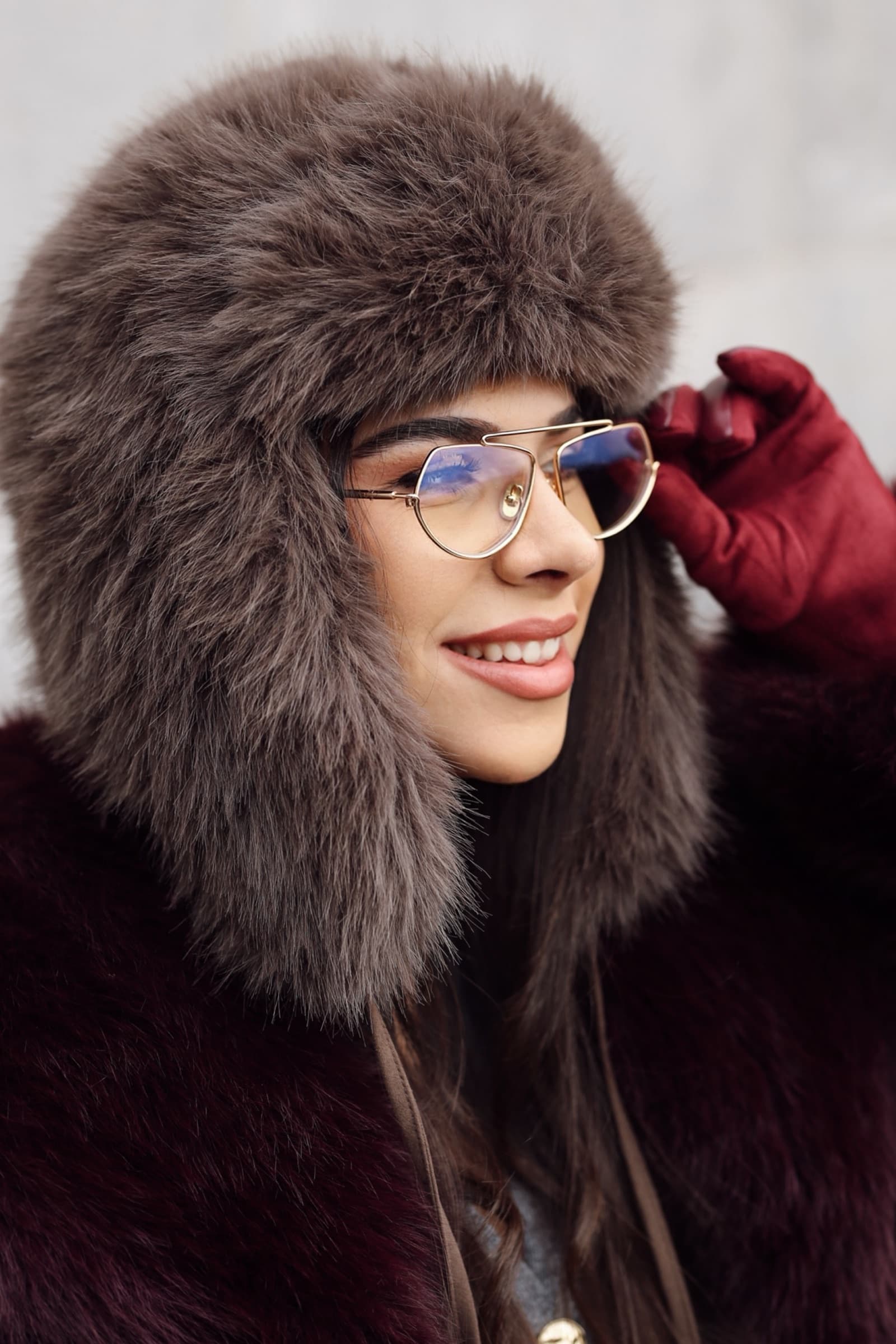 Clear optical frames under a fur hat, red leather gloves