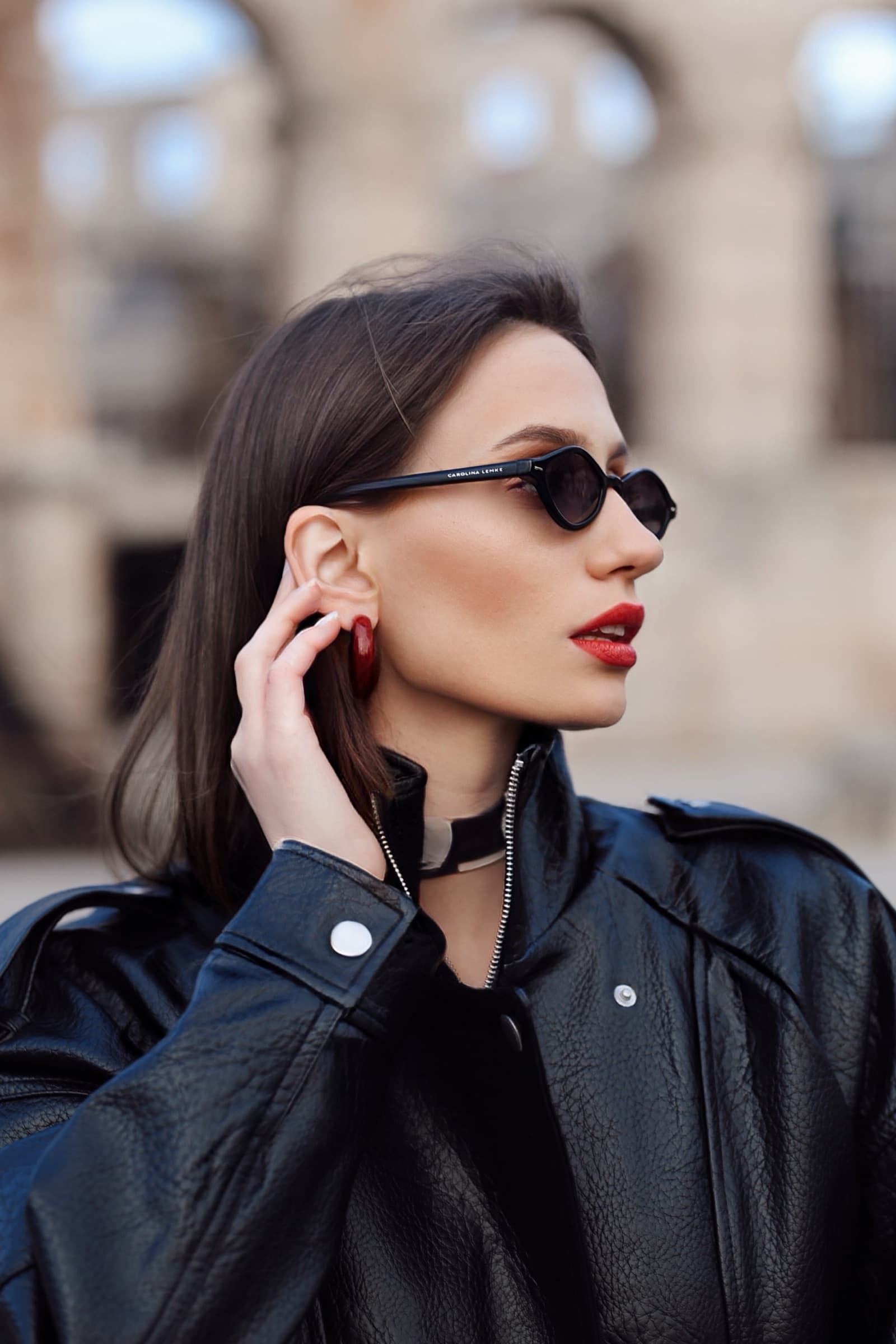 Profile in black leather, hand at the ear, arena behind