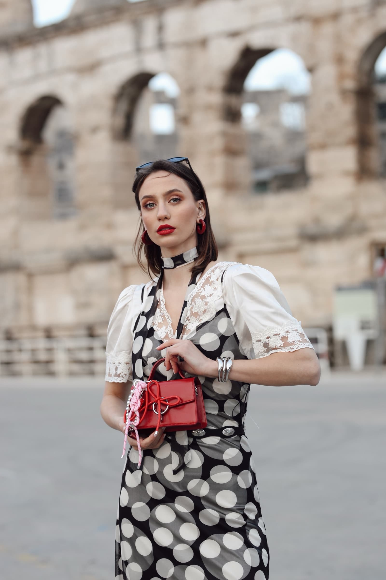Polka-dot dress and red mini bag beneath the arena arches