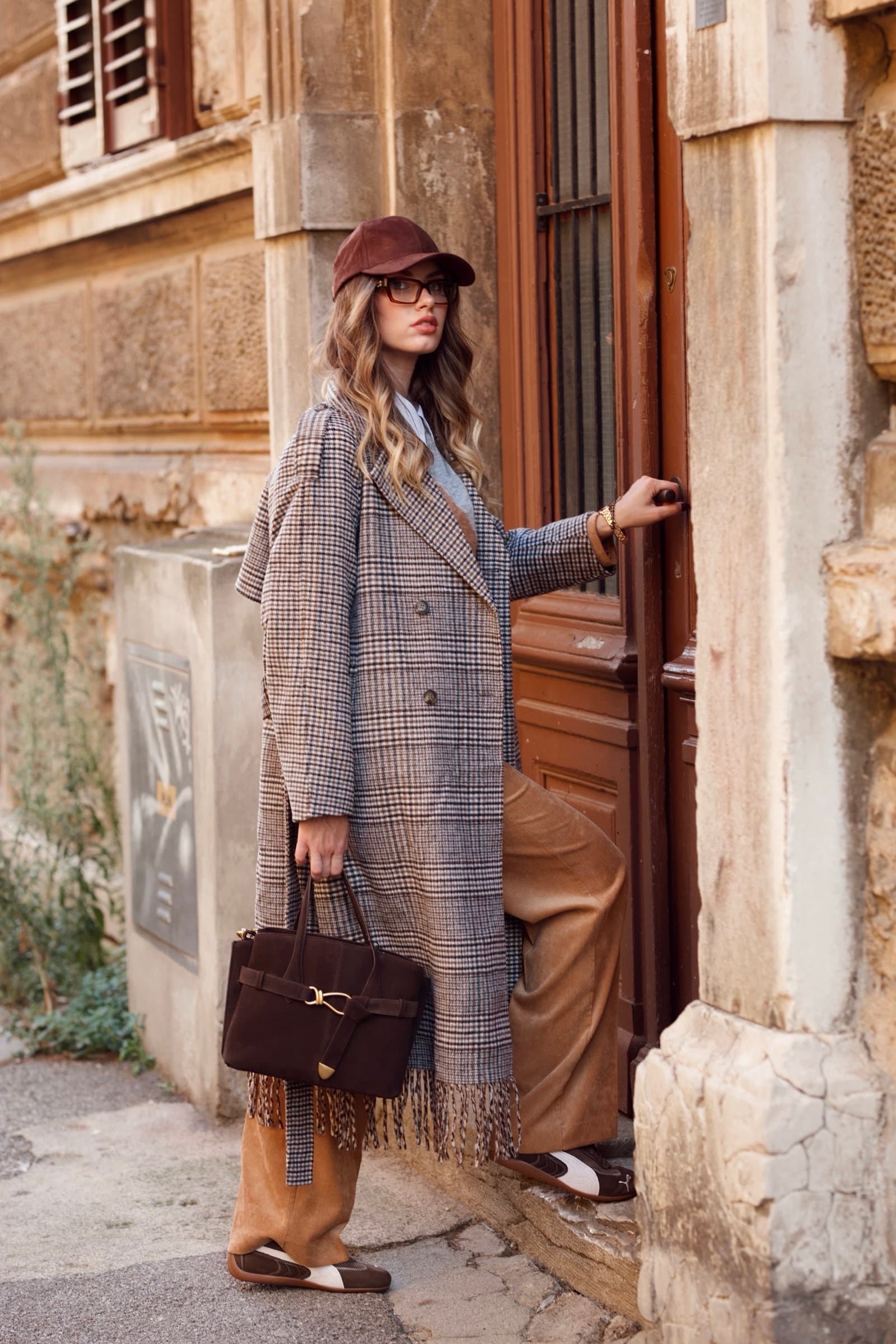 Long check coat and cap in a stone doorway