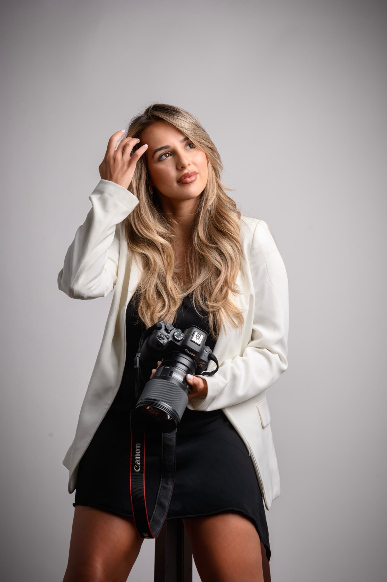 Maja in a white blazer, camera at her side, looking into the light