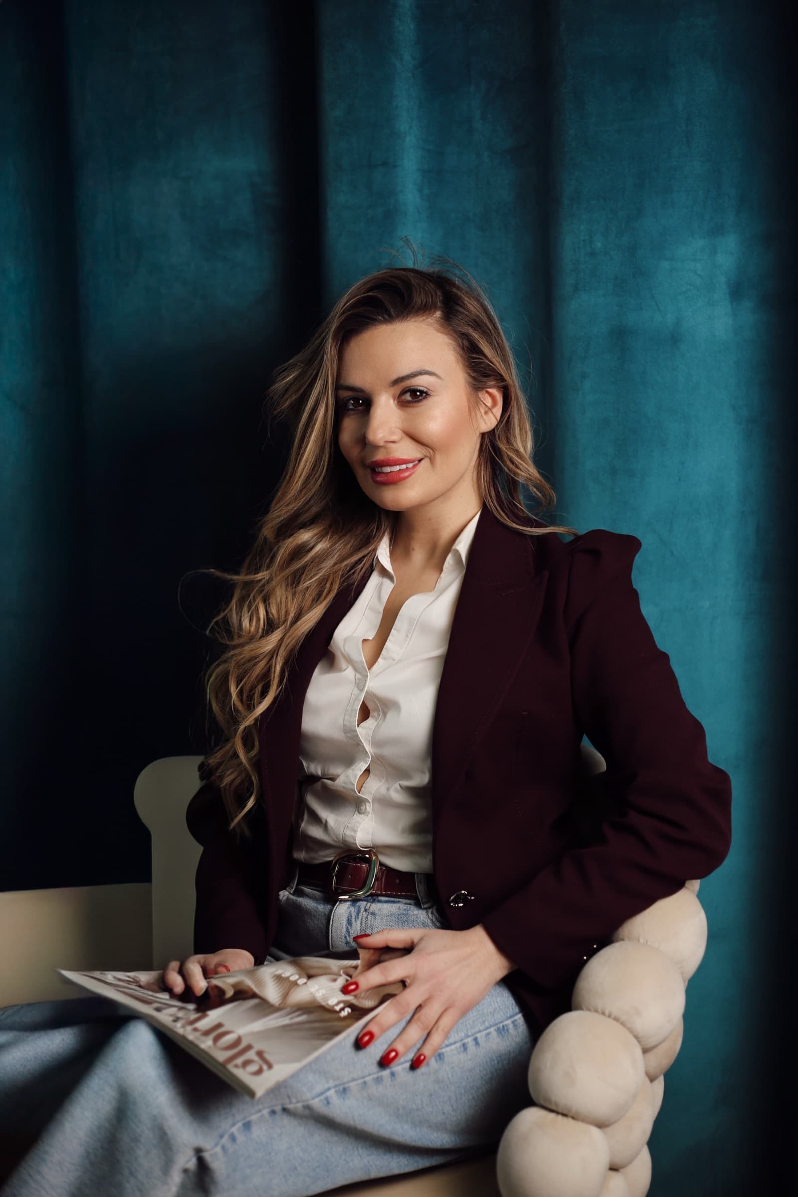 Reading in the armchair, burgundy blazer and teal drape