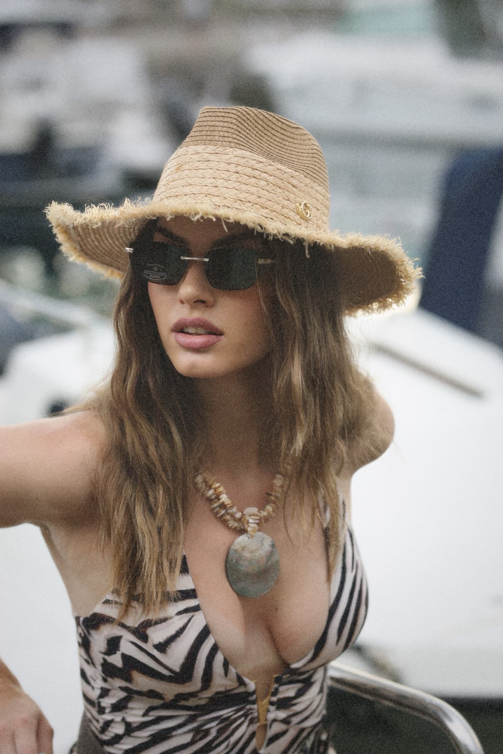 Wide straw hat and a shell pendant, moored boats behind