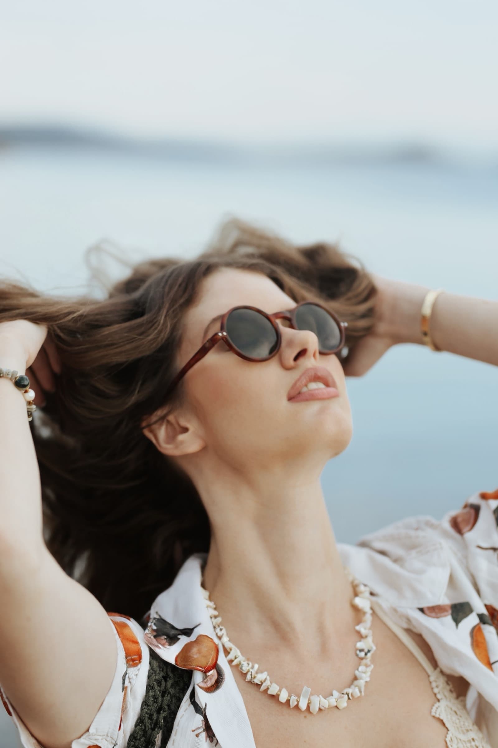 Head tilted back into the sun, round sunglasses and shells