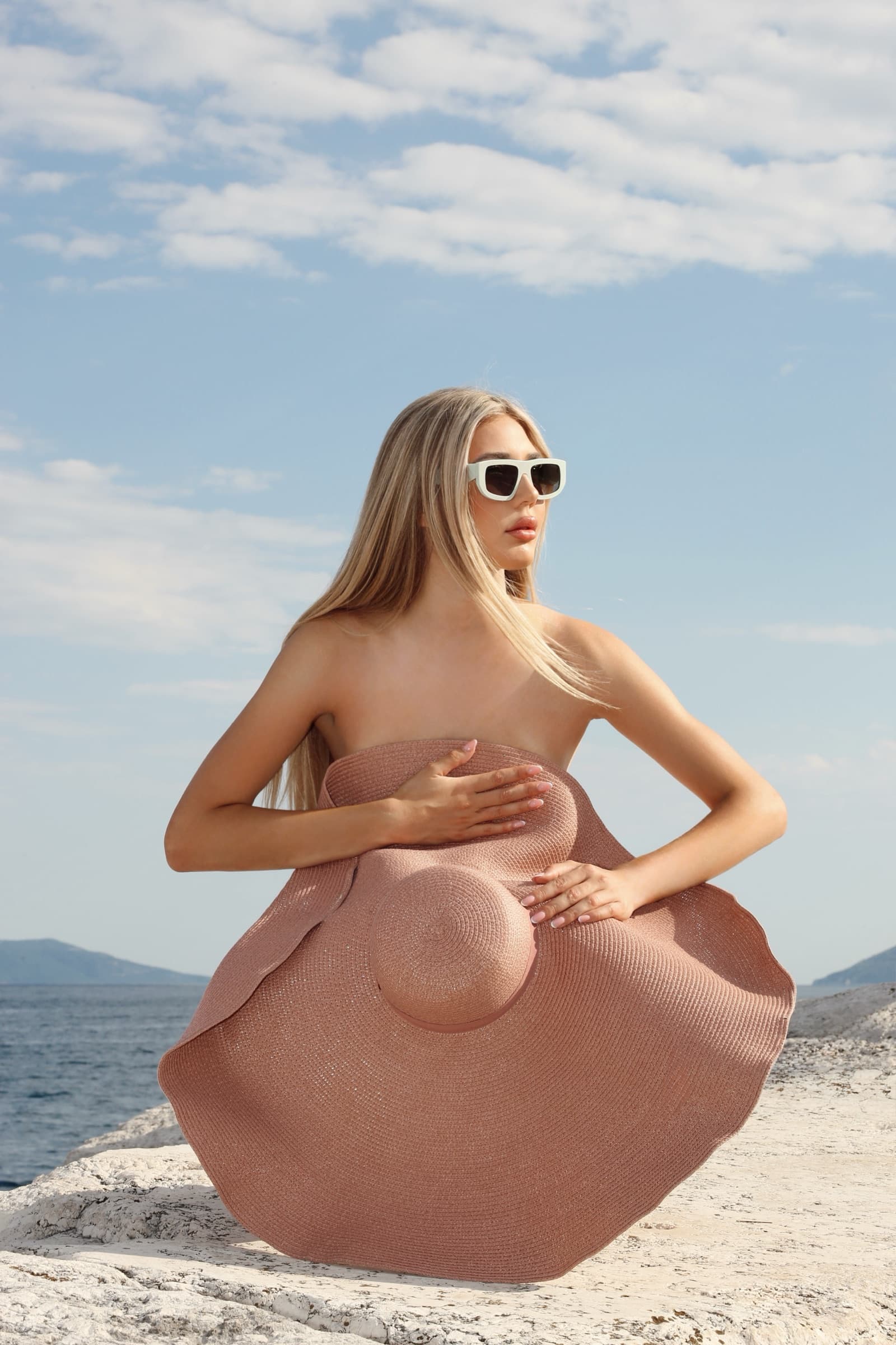 Holding a wide raffia hat against a strapless nude dress