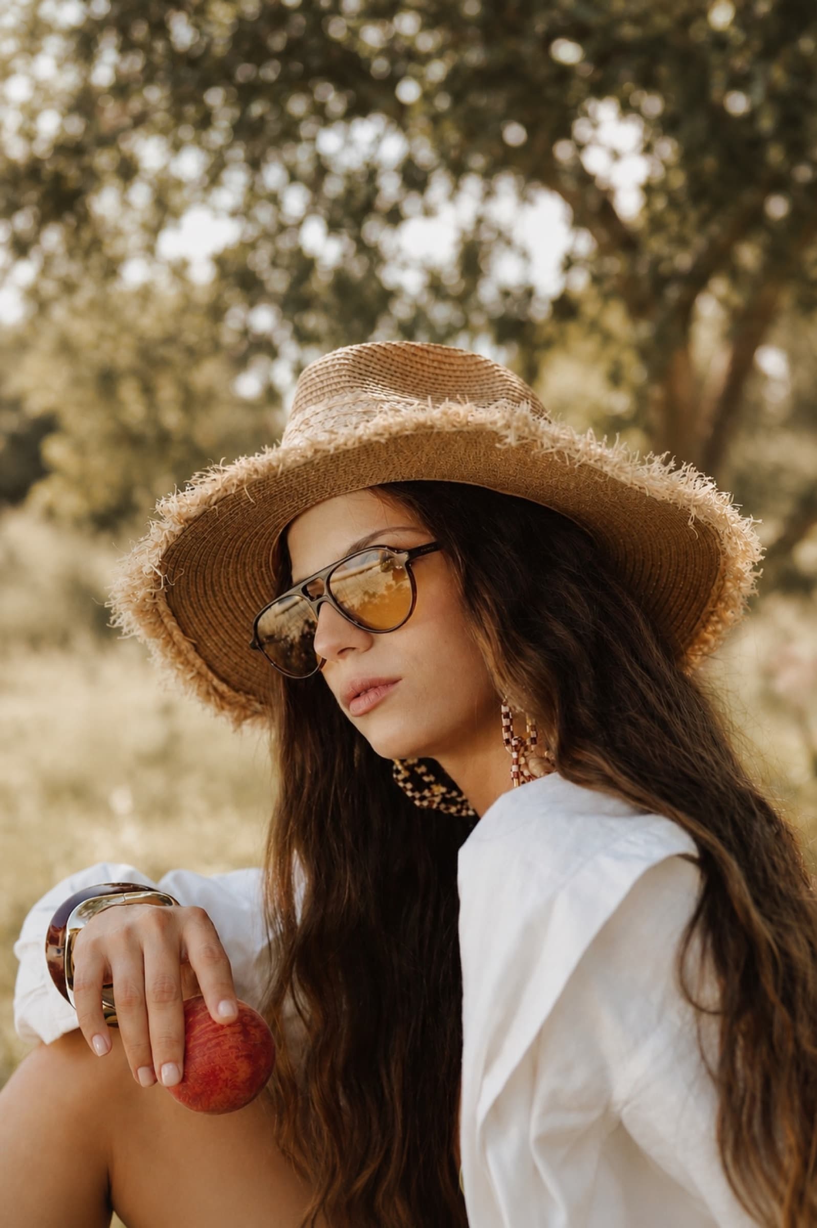 White shirt and straw hat, holding a peach among the olives